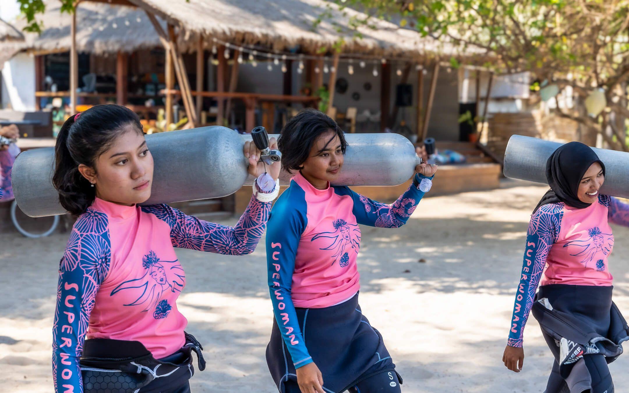 Three divers walk across the beach, oxygen tanks slung across their shoulders, wet suits wrapped around their waists, and eyes trained on the ocean ahead.
Photographer: Valerie Blanchard